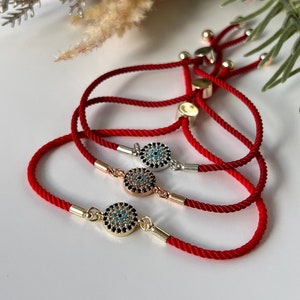 May include: Three red string bracelets with gold and silver charms featuring a blue evil eye design. The charms are adorned with small sparkling stones.