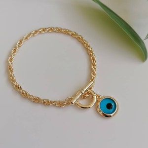May include: A gold chain bracelet with a blue evil eye charm. The chain is a rope style and the charm is round with a black pupil.