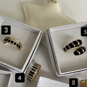 May include: Four black and gold rings displayed in white boxes. The boxes are labeled with numbers 3, 4, 5, and 8.