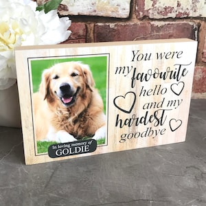 Puede incluir: Un marco de fotos de madera con una foto de un perro golden retriever. El marco tiene el texto "You were my favourite hello &hearts; and my hardest goodbye &hearts;" y "In loving memory of GOLDIE".