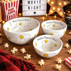 Op de afbeelding: Drie witte keramische kommen met zwarte cursieve tekst en gele popcornillustraties. De grootste kom heeft de tekst Alex's Popcorn Bowl, de middelste Daddy's Popcorn Bowl en de kleinste kom Kiddie's Popcorn Bowl.