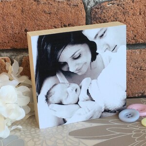 May include: A black and white photo of a couple holding a newborn baby. The photo is printed on a wooden block.