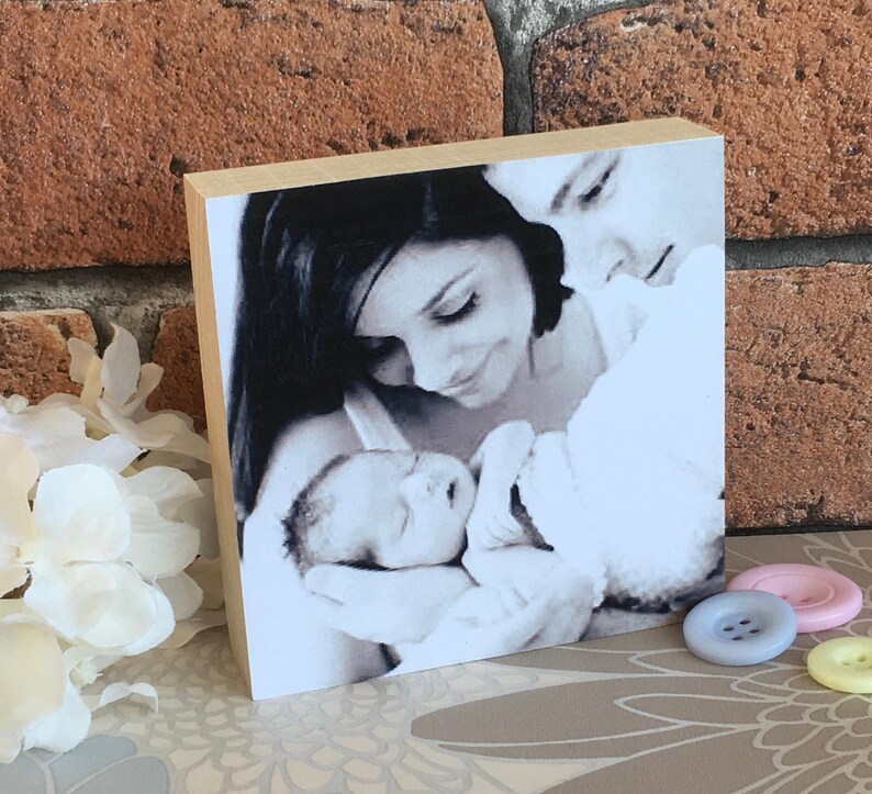 May include: A black and white photo of a couple holding a newborn baby. The photo is printed on a wooden block.