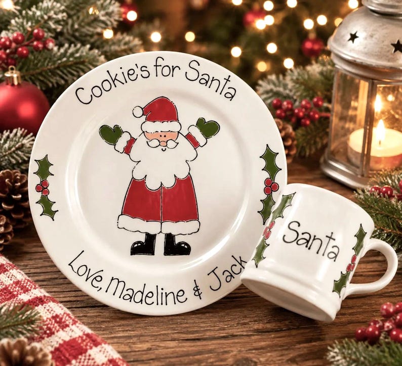 May include: A white ceramic plate and matching mug set featuring a hand-painted Santa Claus illustration. The plate reads Cookie's for Santa and Love, Madeline & Jack. The mug features the word Santa and green holly leaf accents.