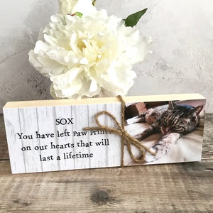 May include: A wooden block with a white background and a photo of a tabby cat. The text "SOX" is printed at the top of the block. The text "You have left paw prints on our hearts that will last a lifetime" is printed below the photo.