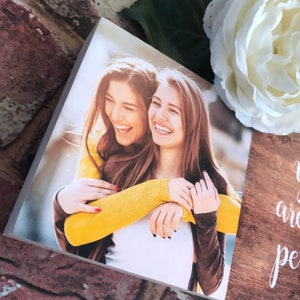 May include: Two women are smiling and hugging each other. They are both wearing casual clothing. The woman in the front is wearing a yellow sweater and the woman in the back is wearing a brown sweater.