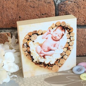 May include: A newborn baby sleeping in a heart-shaped nest made of wooden logs. The baby is wearing a white headband and is surrounded by soft white fabric.