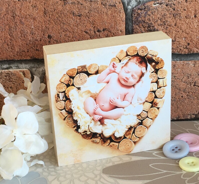 May include: A newborn baby sleeping in a heart-shaped nest made of wooden logs. The baby is wearing a white headband and is surrounded by soft white fabric.