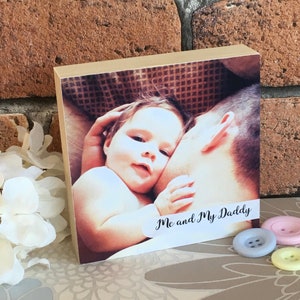 May include: A wooden photo block with a picture of a baby and a man. The baby is lying on the man's shoulder and the text "Me and My Daddy" is printed on the block.