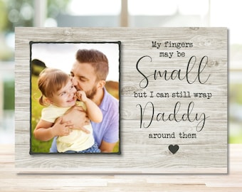 May include: A wood-grain photo frame with a picture of a father and daughter. The text reads "My fingers may be small but I can still wrap Daddy around them".