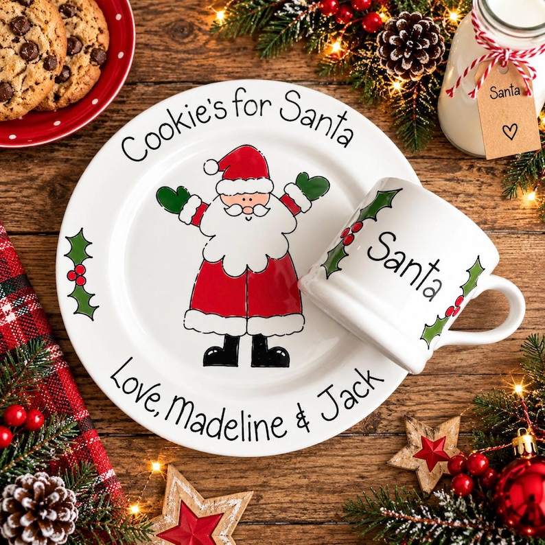May include: A white ceramic plate and matching mug set featuring a cartoon Santa Claus illustration. The plate is inscribed with "Cookie's for Santa" and "Love, Madeline & Jack," while the mug features the word "Santa" and green holly.