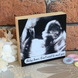May include: A wooden block with a black and white ultrasound image of a baby. The text "Baby Jones. Can't wait to meet you" is printed on the block.