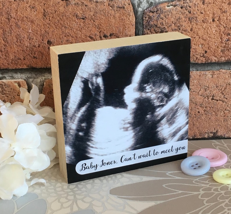 May include: A wooden block with a black and white ultrasound image of a baby. The text "Baby Jones. Can't wait to meet you" is printed on the block.