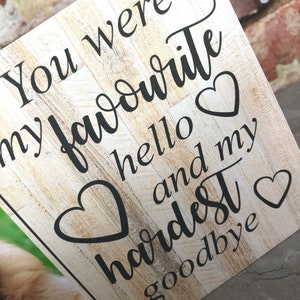 Puede incluir: Un letrero de madera con fondo blanqueado y texto negro que dice "You were my favourite hello and my hardest goodbye". El letrero tiene dos corazones negros.