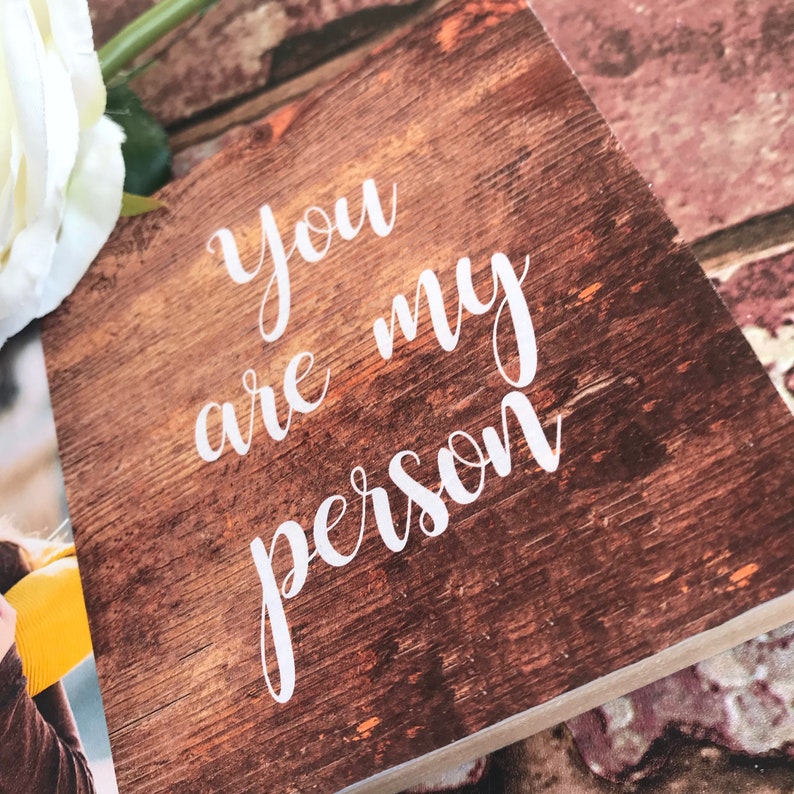 May include: A wooden sign with a rustic brown finish and white lettering that reads "You are my person".