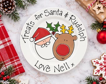 May include: A white ceramic plate featuring a cartoon illustration of Santa Claus and a reindeer with a red nose. The text reads "Treats for Santa & Rudolph" and "Love Nell". The design includes green holly leaves and yellow antlers.