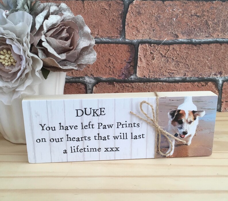 May include: A wooden memorial plaque with a white background and black text that reads "DUKE You have left Paw Prints on our hearts that will last a lifetime xxx". A photo of a dog is on the right side of the plaque.