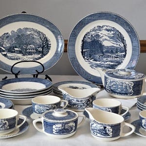 May include: A complete blue and white dinnerware set featuring landscape scenes. The set includes plates, bowls, cups, saucers, a teapot, creamer, and sugar bowl. The plates have a decorative border.