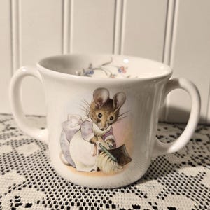 May include: A white ceramic mug with a black handle and the text "But First, Coffee" in a black, handwritten-style font. The mug is on a white surface.