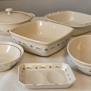 May include: A collection of off-white ceramic serving dishes. The set includes a lidded casserole dish, a square baking dish, a rectangular baking dish, two bowls, and a small divided dish. Each piece is decorated with a blue floral and scroll design.