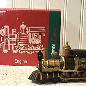 May include: A decorative model train engine with gold and black accents. The train is next to a red box with a line drawing of a train and the word "Engine". The box also has the text "Towne Express".