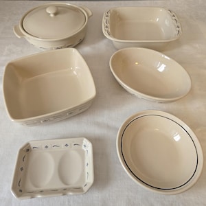 May include: A collection of off-white ceramic serving dishes. The set includes a covered casserole dish, rectangular baking dishes, an oval serving bowl, and a divided dish. Each piece has a blue floral design.