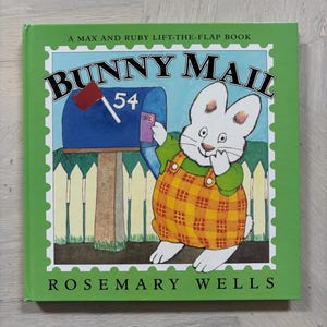 May include: A children's book titled "Bunny Mail" by Rosemary Wells. The cover features a cartoon bunny in overalls, posting a letter in a blue mailbox. The book has a green border with the text "A Max and Ruby Lift-the-Flap Book".