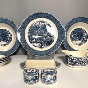 May include: A collection of cream-colored ceramic dinnerware featuring blue transferware patterns. The set includes a large handled platter, two bowls, a gravy boat, a butter dish, and two shakers marked with S and P.