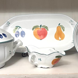 May include: A white ceramic serving set featuring a fruit design. The set includes a lidded soup tureen, a serving platter, a gravy boat, and a round bowl. Each piece is decorated with colorful illustrations of plums, peaches, and pears, with green trim.
