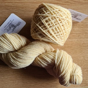 May include: Two skeins of pale yellow yarn, one wound into a ball and the other loose, with a white label that reads "Smoochie Sheep" and "Superwash Merino Wool Yarn".