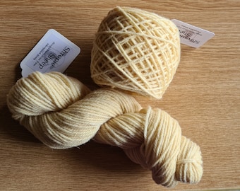 May include: Two skeins of pale yellow yarn, one wound into a ball and the other loose, with a white label that reads "Smoochie Sheep" and "Superwash Merino Wool Yarn".