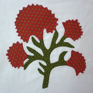 May include: A green fabric applique of a tree with three red and yellow floral blooms. The tree has a dotted pattern and the blooms have a small floral pattern.