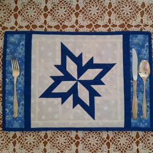 May include: Blue and white quilted placemat with a star design and a silver fork and spoon on the side.