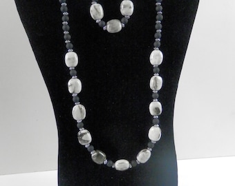 May include: A black and white beaded necklace and bracelet set. The necklace and bracelet are made with oval-shaped white beads with black accents and black beads.