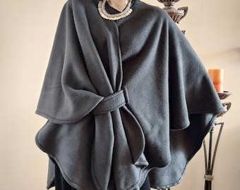 May include: A dark gray fleece cape with a self-tie closure. The cape is worn by a person and has a decorative silver necklace.