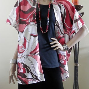 May include: A white, pink, and brown patterned kimono-style cardigan with short sleeves. The cardigan is open in the front and has a black top and black skirt underneath.