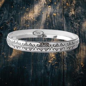 Pode incluir: Uma pulseira de prata com um padrão geométrico gravado. A pulseira tem um acabamento polido e é marcada com "STERLING". O design apresenta formas e linhas repetidas ao redor da pulseira, criando um acessório decorativo.