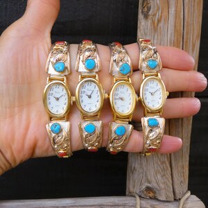May include: Four gold-toned watches with oval faces and turquoise accents. The watch bands feature ornate designs and red and turquoise stones. The watch faces have black numerals and hands.