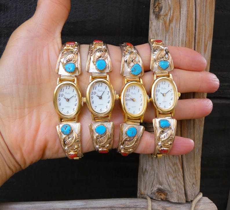 May include: Four gold-toned watches with oval faces and turquoise accents. The watch bands feature ornate designs and red and turquoise stones. The watch faces have black numerals and hands.