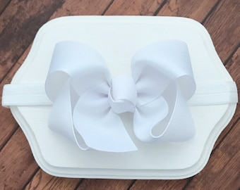 May include: White satin bow headband. The bow is tied in a large, classic shape. The headband is made of elastic.