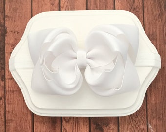 May include: White satin hair bow with a large, curled design, attached to a white elastic headband.  Stephanie's Bows.