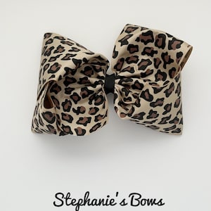 May include: A large brown and black leopard print hair bow. The bow is tied with a black ribbon.