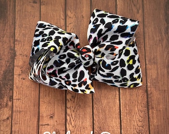 Könnte beinhalten: Eine große weiße Schleife mit einem schwarzen und regenbogenfarbenen Leopardenmuster. Die Schleife ist aus Grosgrainband gefertigt und hat einen drahtverstärkten Rand.