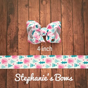 May include: A 4-inch hair bow with a white background and a pattern of pink Christmas trees, teal stars, and teal trees. The bow is on a wooden surface. The text "Stephanie's Bows" is at the bottom.