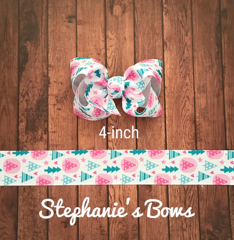 May include: A 4-inch hair bow with a white background and a pattern of pink Christmas trees, teal stars, and teal trees. The bow is on a wooden surface. The text "Stephanie's Bows" is at the bottom.