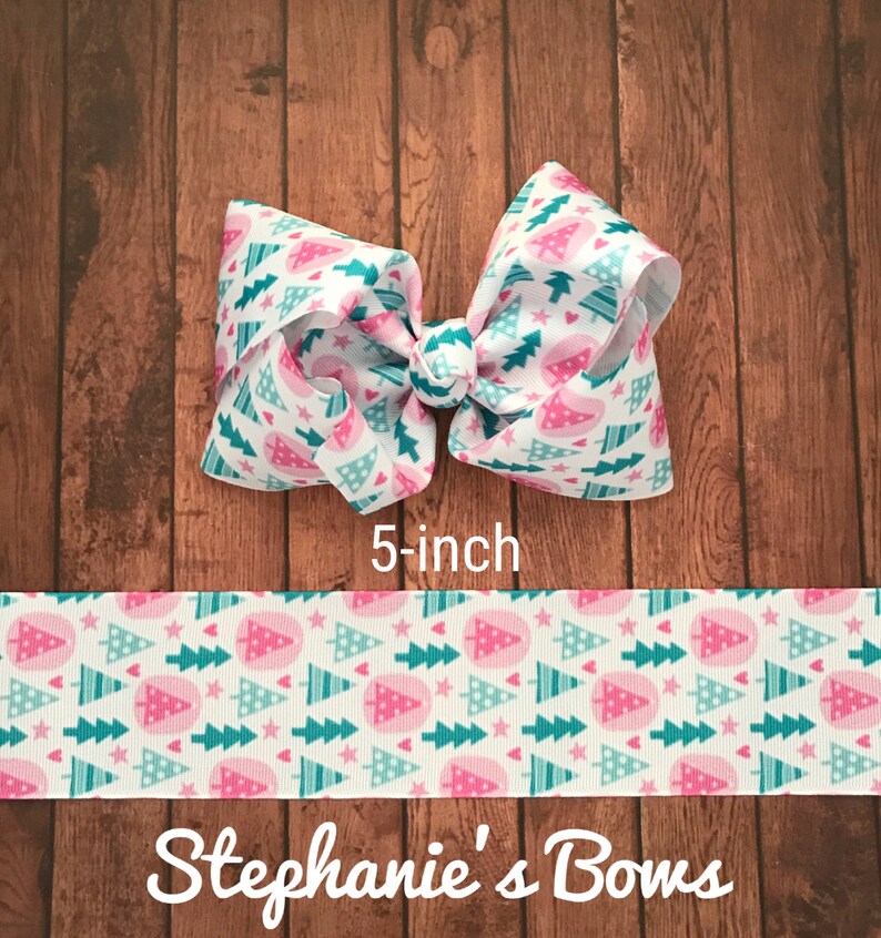 May include: A 5-inch hair bow with a white background and a repeating pattern of pink and teal Christmas trees and stars. The bow is tied in the center. The text "Stephanie's Bows" is at the bottom.