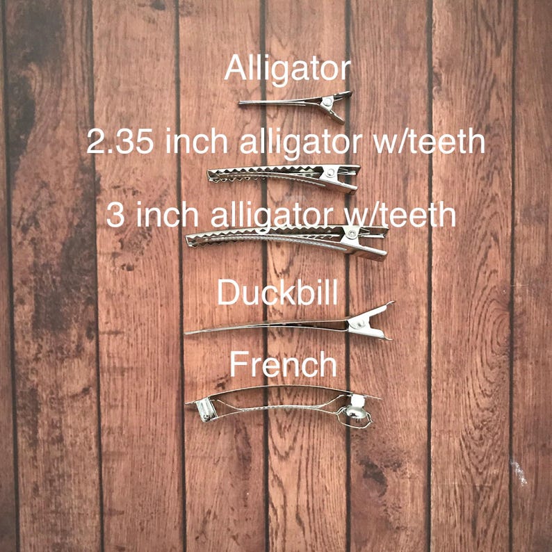 May include: A set of five hair clips in different sizes and styles, including alligator clips with teeth, a duckbill clip, and a French clip. The clips are silver-toned and arranged vertically on a wooden background.