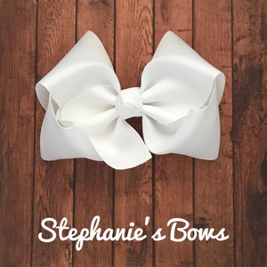 May include: A large white satin bow, tied in a classic shape. The bow is displayed against a woodgrain background.