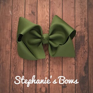 May include: A large green bow made from grosgrain ribbon. The bow is tied in a classic style with a center knot. The bow is photographed against a woodgrain background.