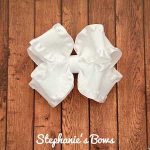May include: A large white bow with a ruffled edge. The bow is made of a soft, silky fabric.